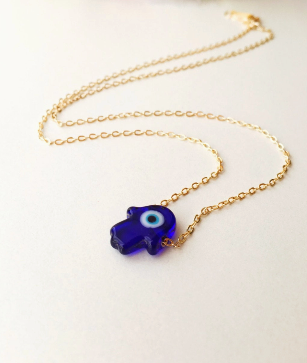 Gold necklace with a blue evil eye pendant on a white background